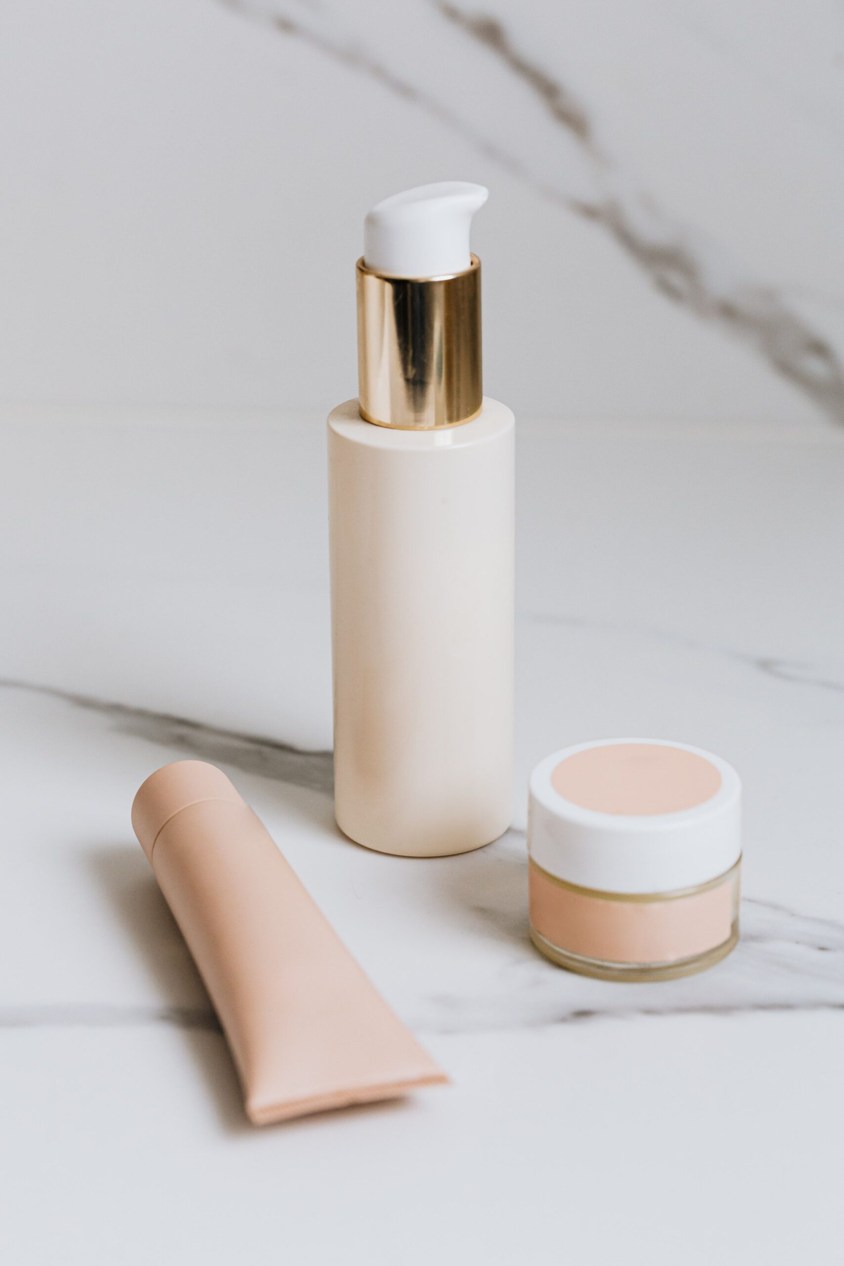 Facial skincare products including a pump bottle, cream jar, and tube displayed on a marble countertop